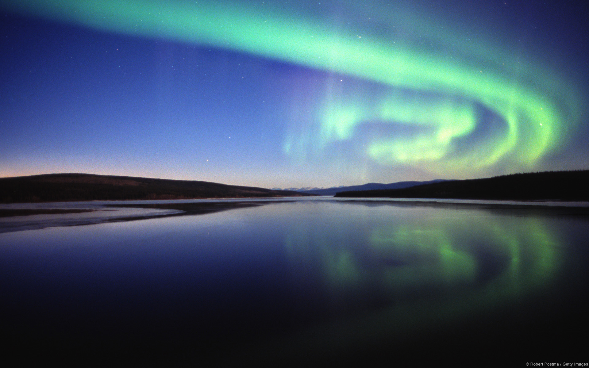 Rio azul escuro sob dois belos arcos verdes de aurora boreal.