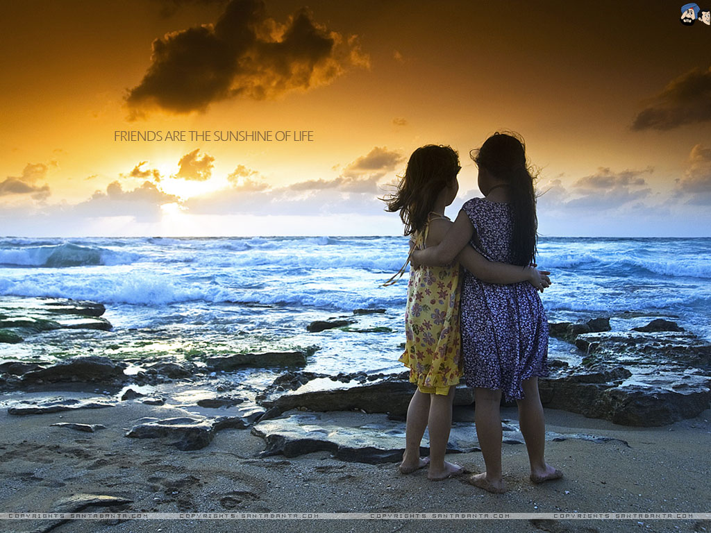 Duas meninas abraçadas à beira do mar com um lindo crepúsculo ao fundo.