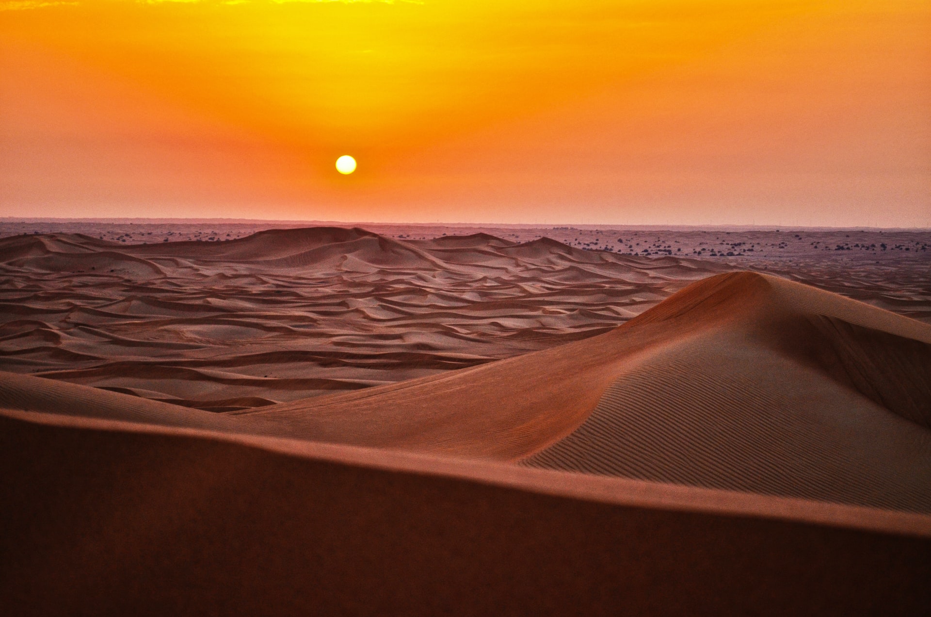 Imagem de um vasto deserto com o Sol e o céu laranjas ao fundo