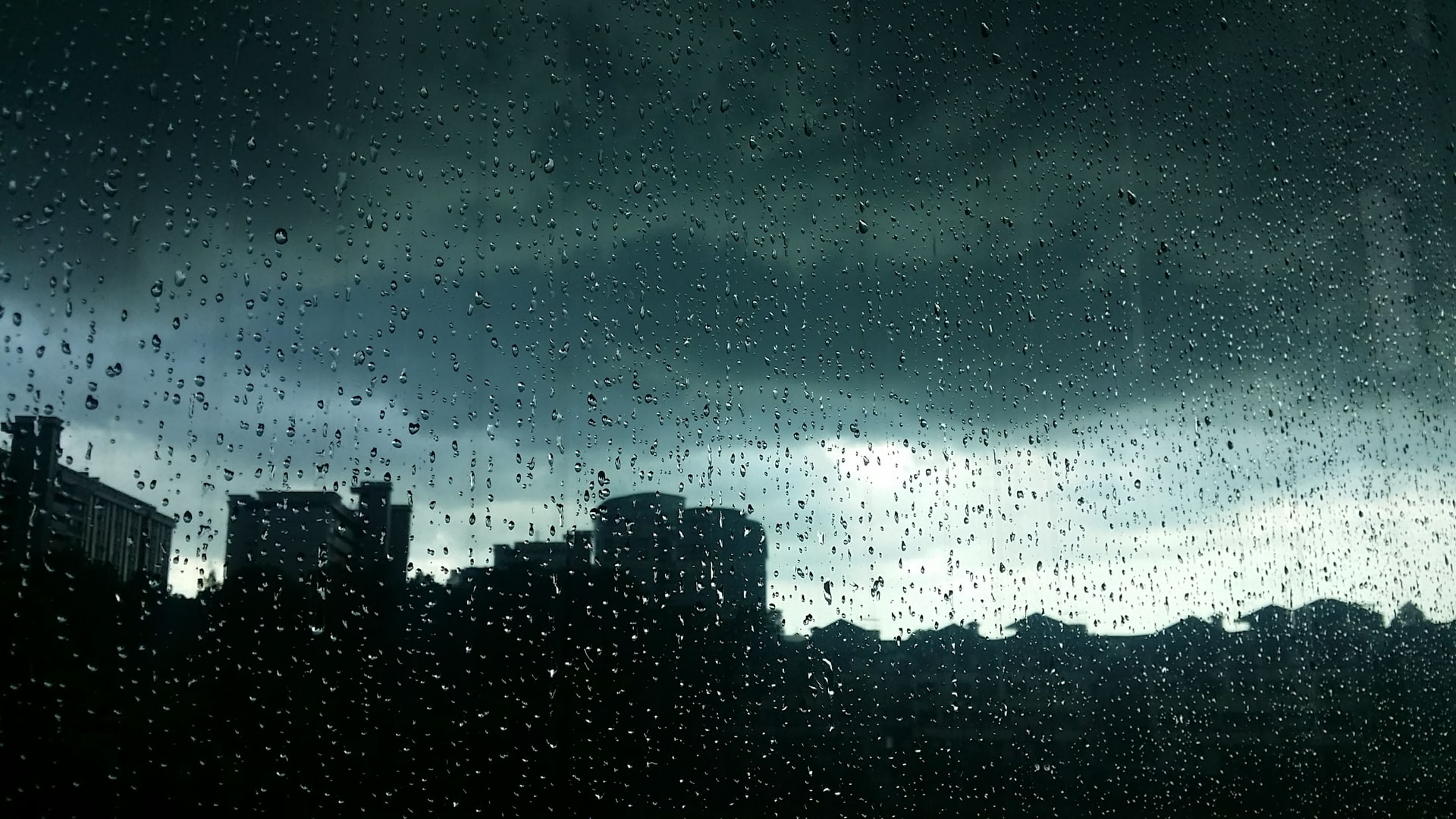 Silueta de edifícios atrás de uma vidro chapiscado de chuva