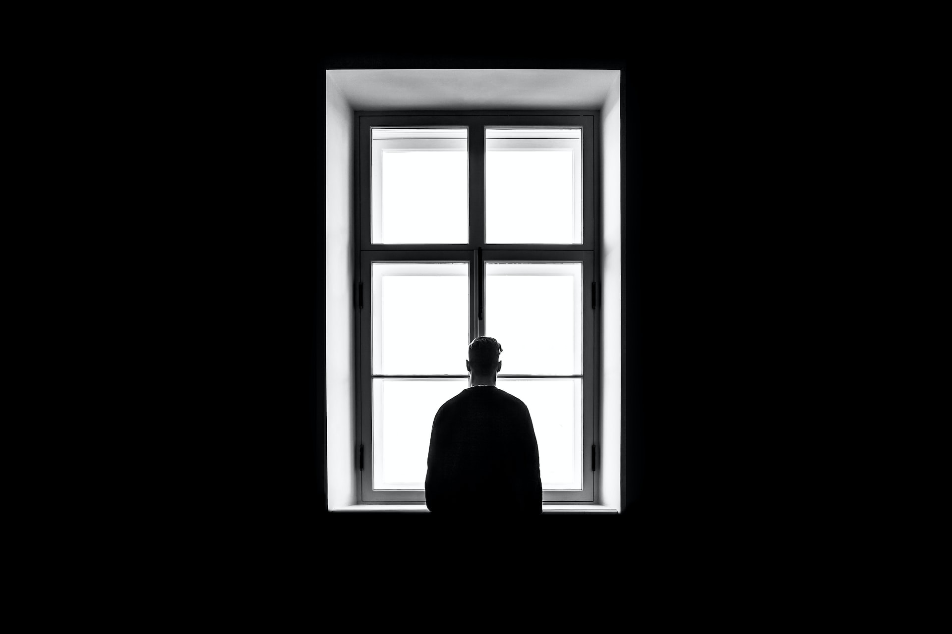 Pessoa observando por uma janela em fundo preto.